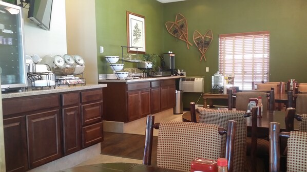A restaurant with a kitchen area, wooden cabinets, and a dining area with checkered chairs.