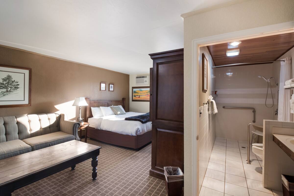 A hotel room with a bed, a sofa, a wooden cabinet, a bathroom with a shower, and a tiled floor.