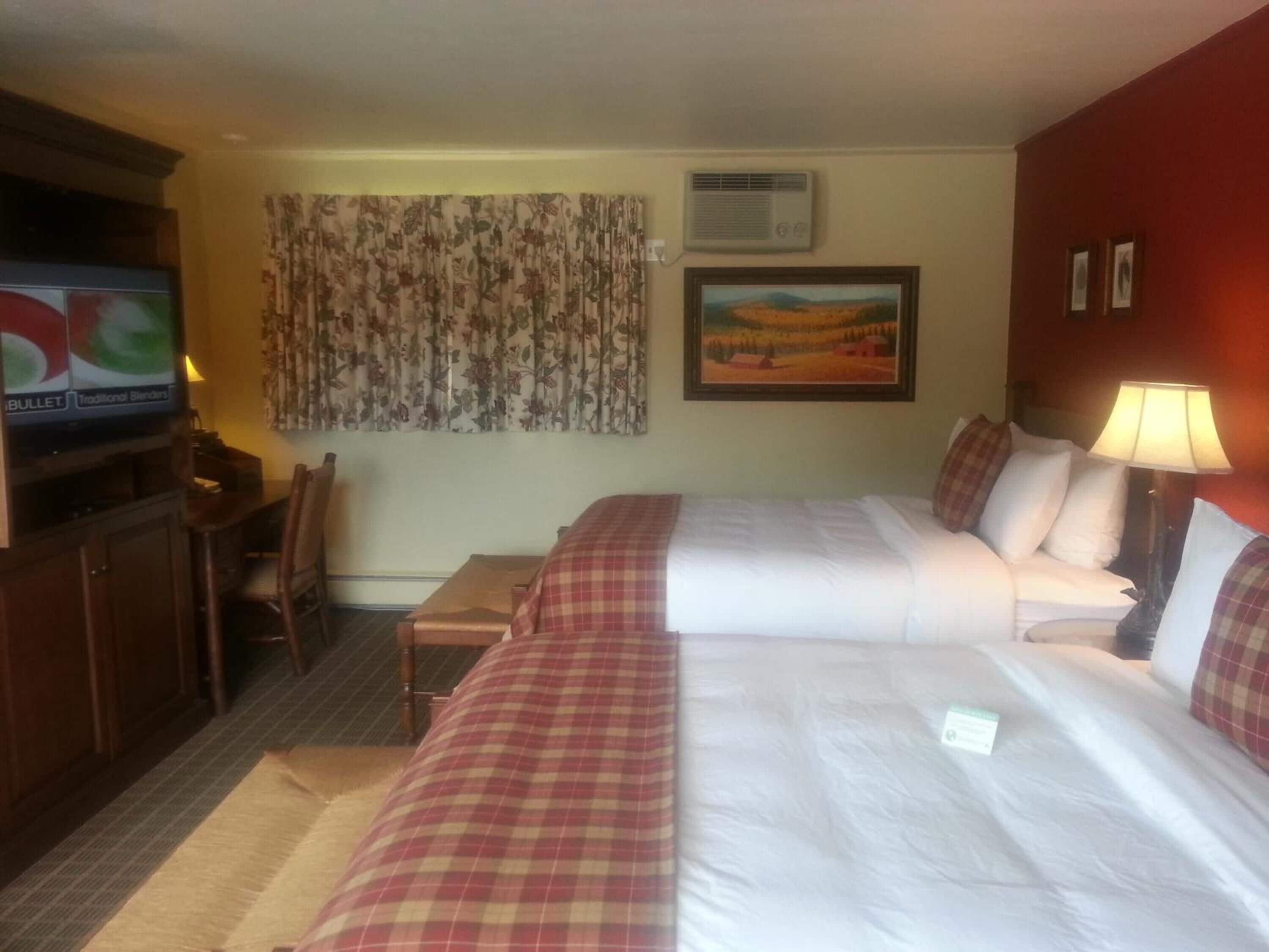 Ett hotellrum med två sängar, en tv, en tavla och ett skrivbord med en stol.