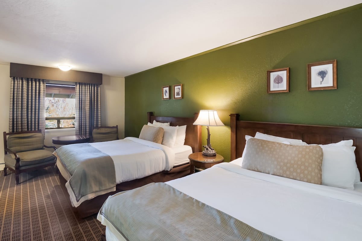 A hotel room with two beds, a chair, a nightstand with a lamp, and framed pictures on the wall.