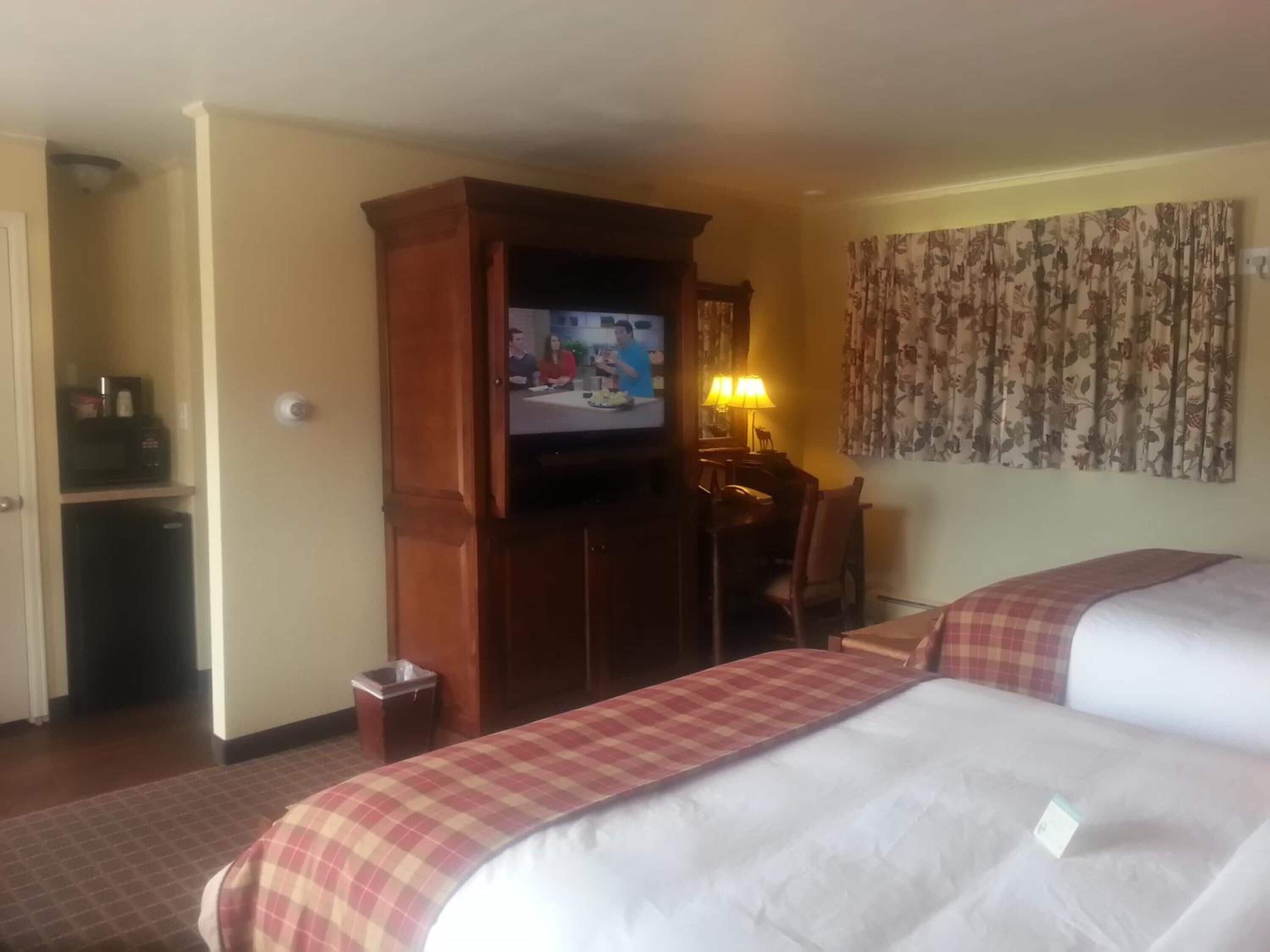 A hotel room with two beds, a television, a desk with a chair, and a lamp.