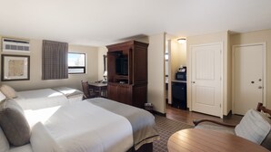 Een hotelkamer met twee bedden, een bureau, een stoel, een televisie en een kitchenette.