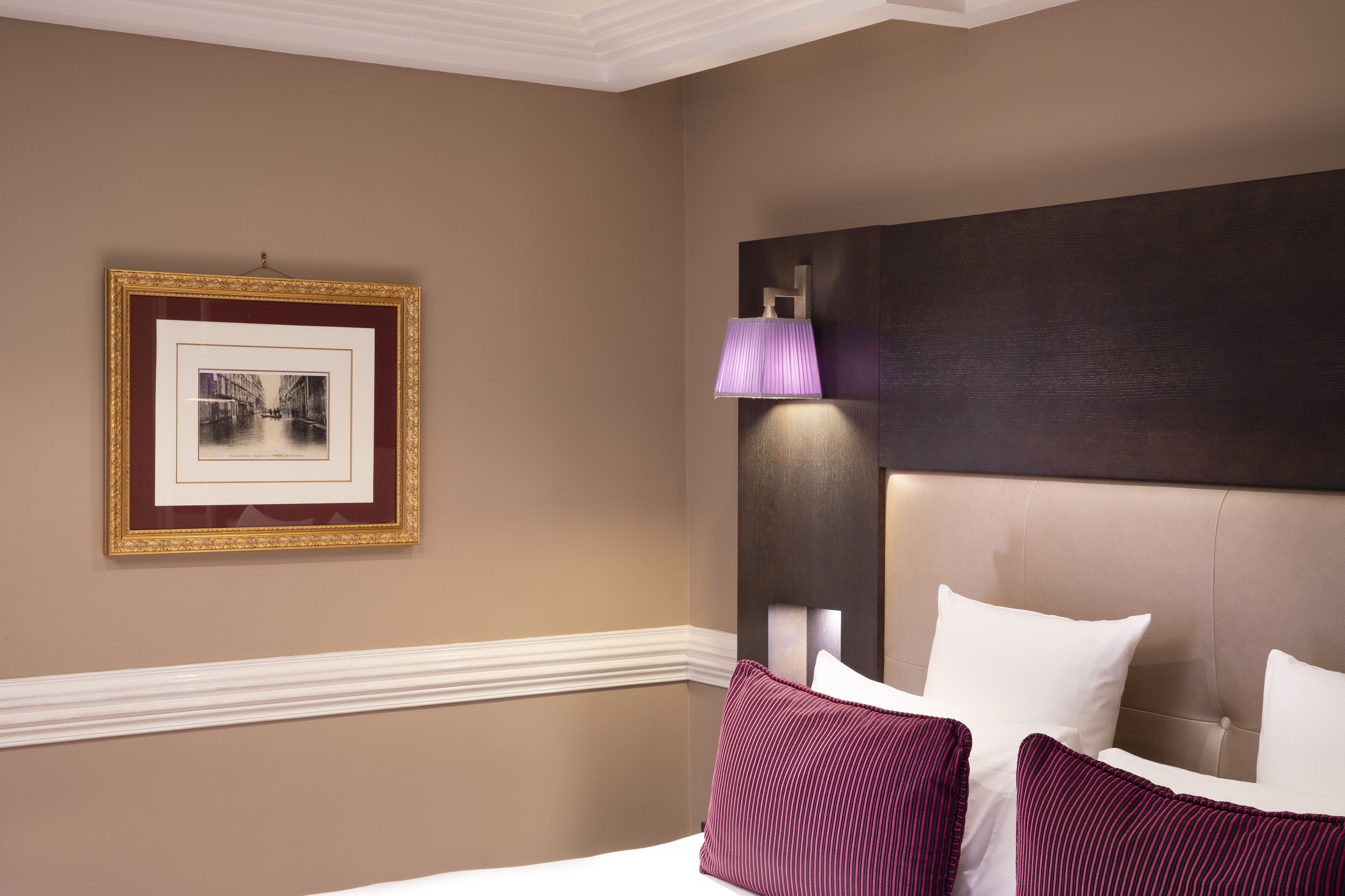 A hotel room with a bed, a framed picture on the wall, and a wall-mounted lamp.