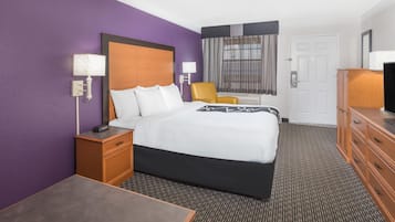 A hotel room with a bed, a desk, a chair, a dresser, and a television.