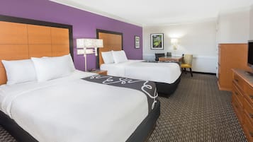 Quarto de hotel com duas camas, uma escrivaninha, uma cadeira, uma televisão e um abajur.