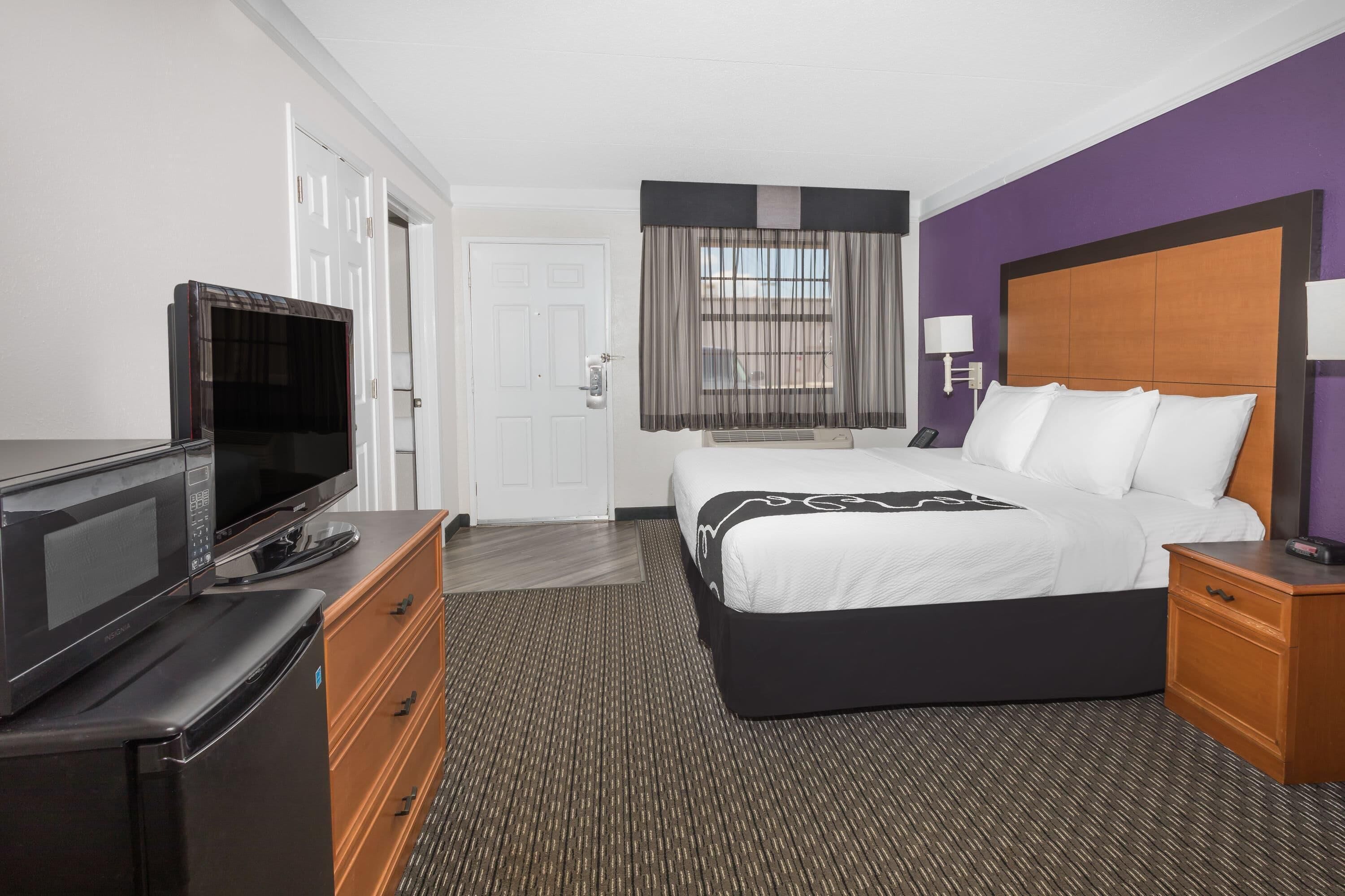 A hotel room with a bed, a TV, a dresser, and a window with curtains.
