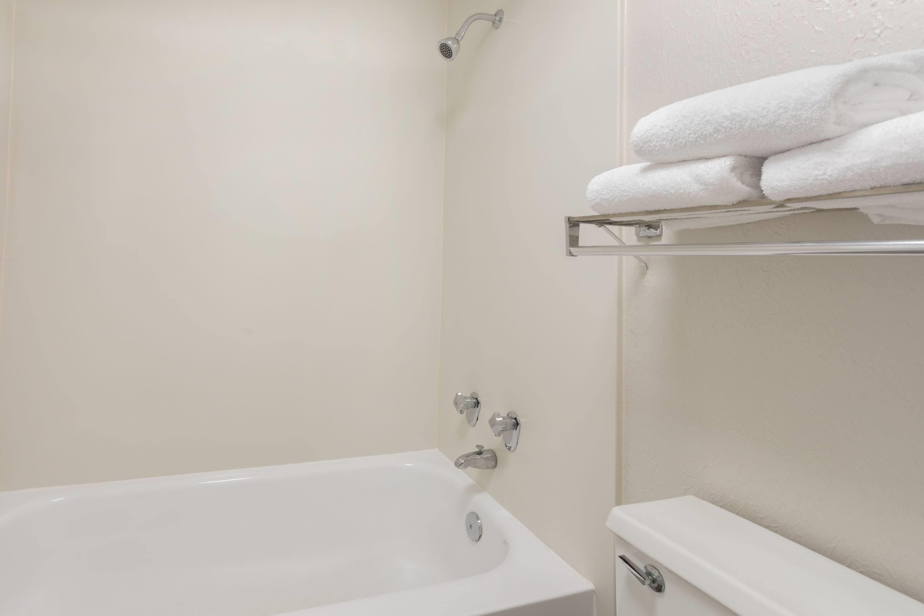 Ein Badezimmer mit einer weißen Badewanne, einer Duschbrause und einem Handtuchhalter mit gefalteten Handtüchern.