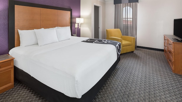 A hotel room with a large bed, a chair, a TV, and a desk.