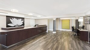 A reception area with a dark wood reception desk, a large white lotus artwork, and a herringbone-patterned floor.