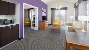 A hotel room with a kitchenette, a dining area, a sofa, a chair, and a ceiling fan.