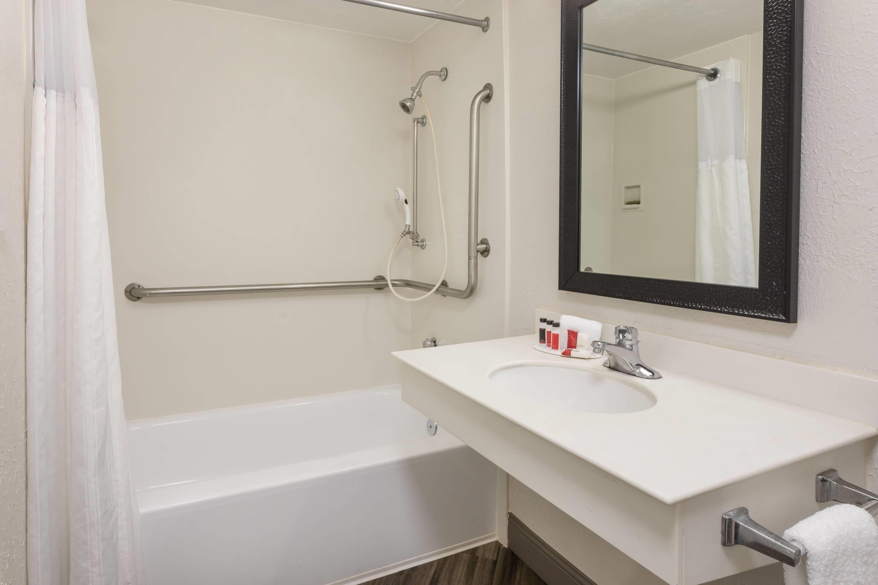 A bathroom with a bathtub, a sink, a mirror, and grab bars.