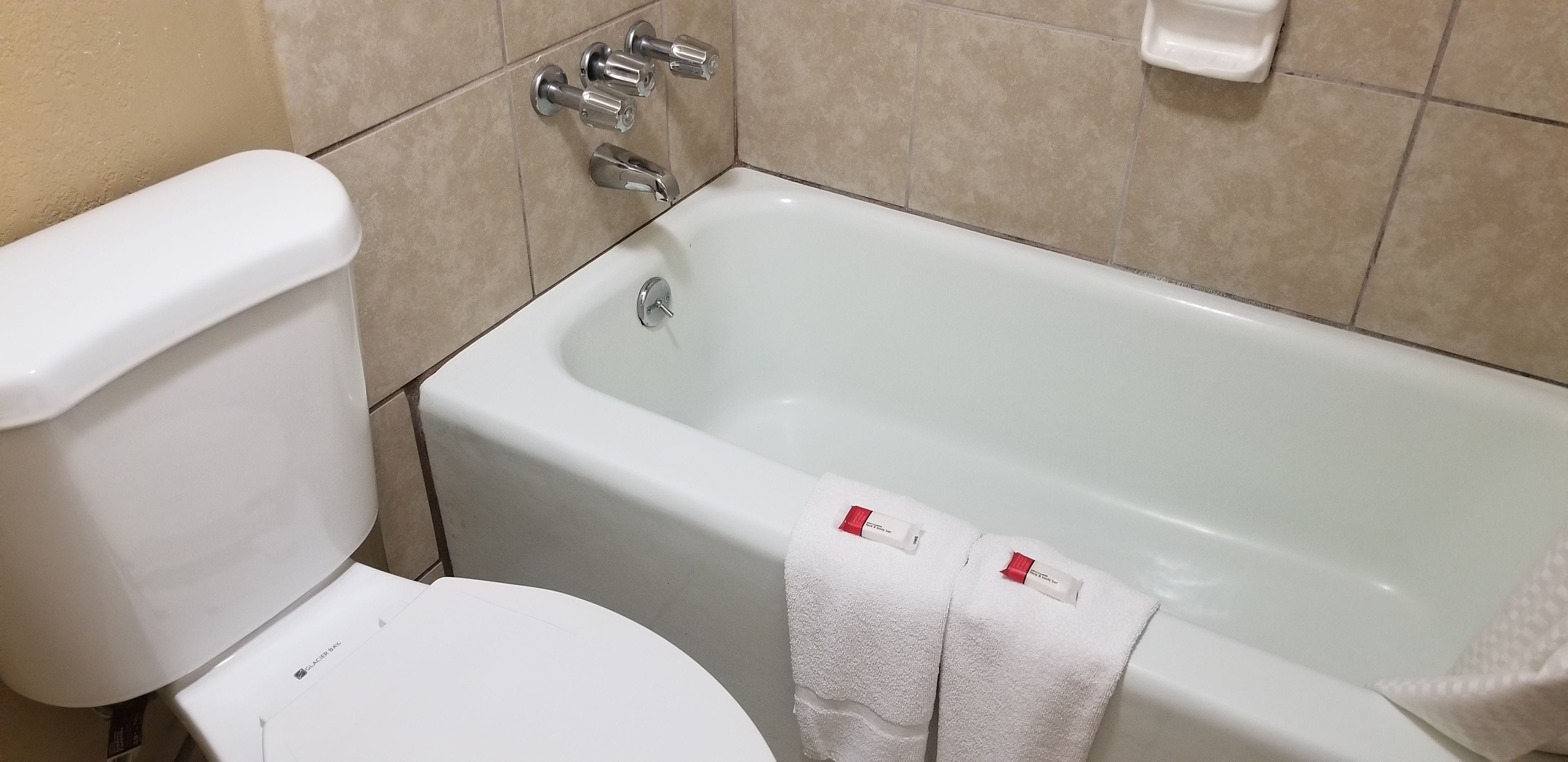 A bathroom with a white toilet, a bathtub with two towels, and a toilet paper holder on the wall.