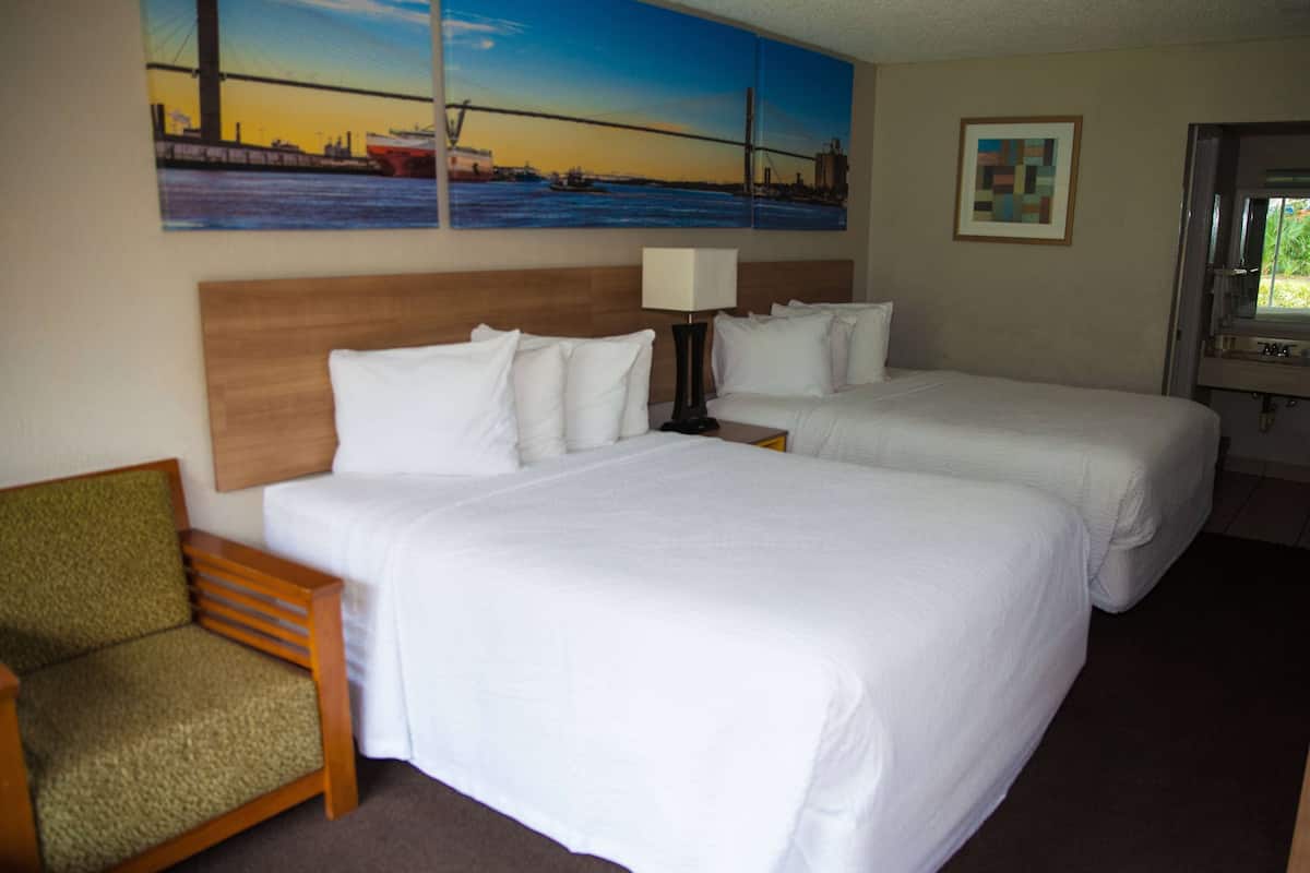 Een hotelkamer met twee bedden, een stoel, een nachtkastje met een lamp en kunstwerken aan de muur.