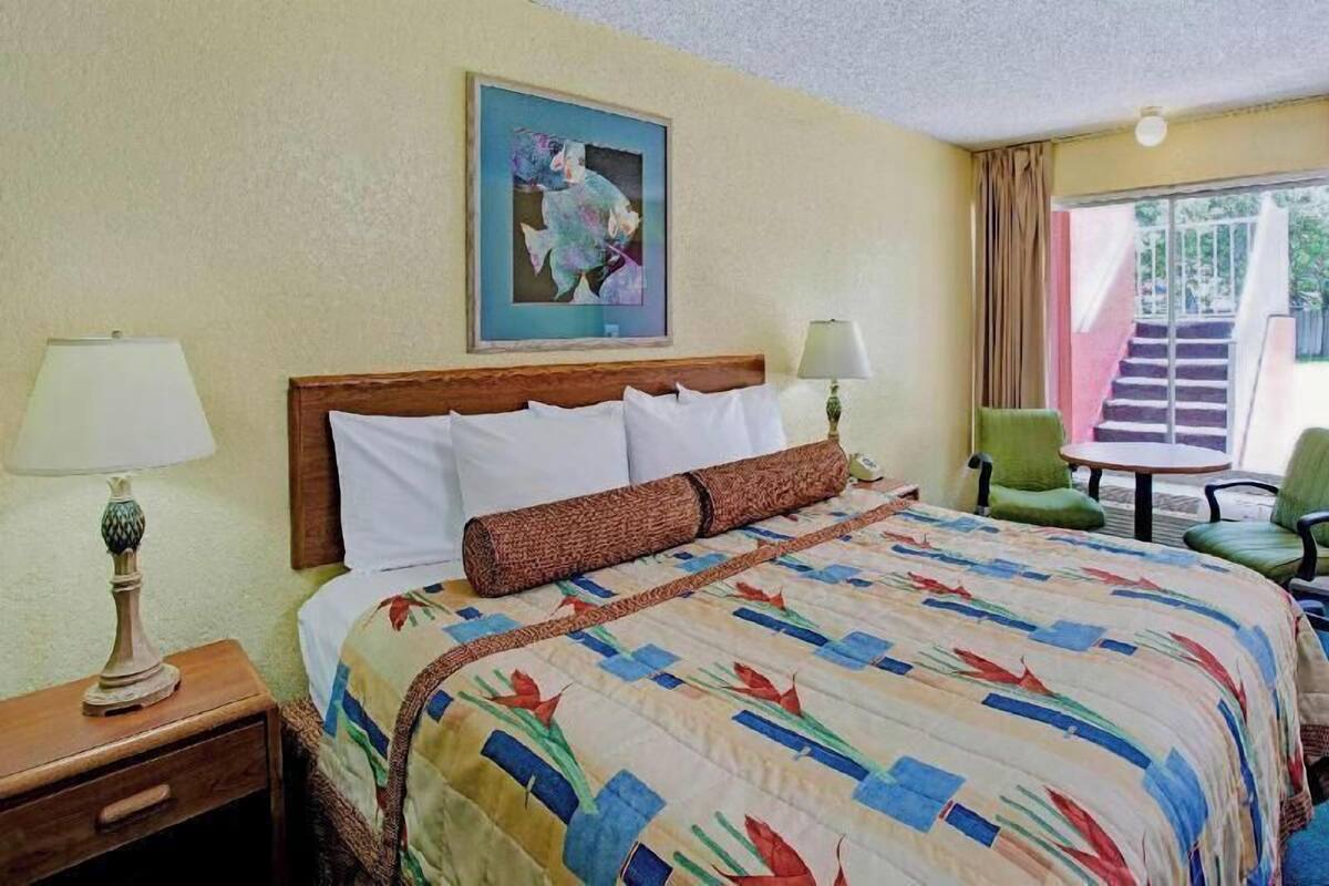 Een hotelkamer met een bed, twee bedlampen, een groene fauteuil, een tafeltje en een schilderij aan de muur.