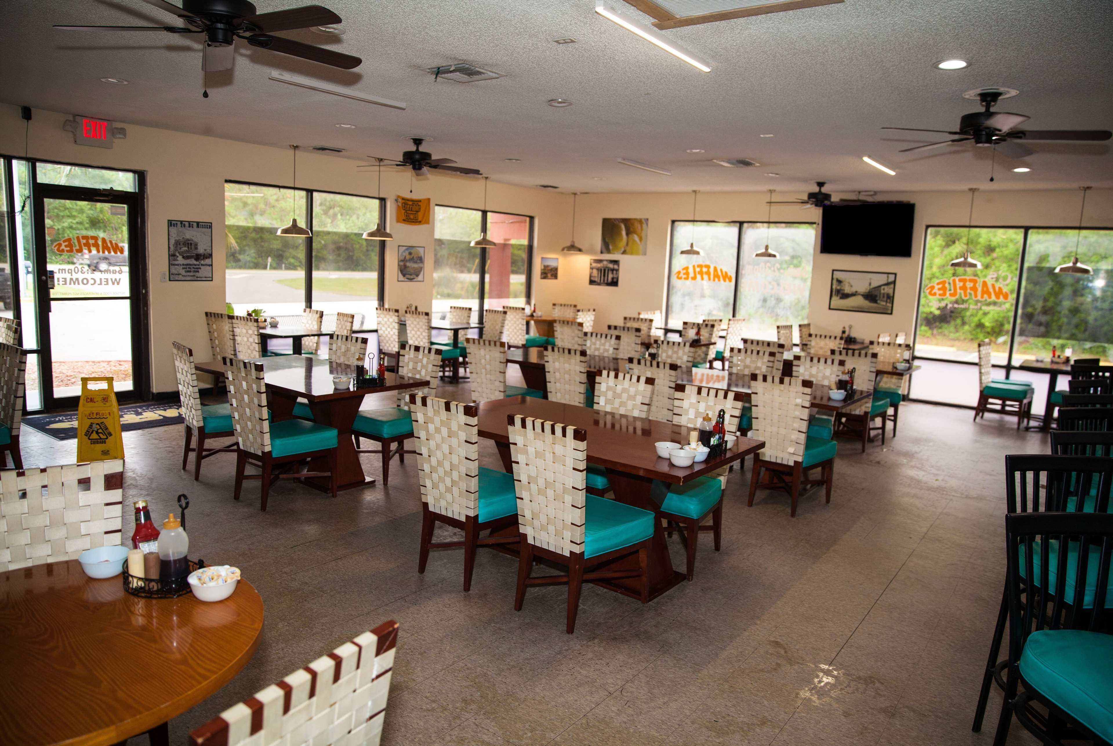 A restaurant with multiple dining tables and chairs, ceiling fans, and large windows.