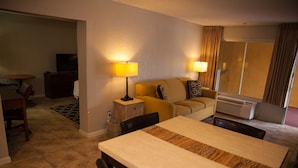 Habitación de hotel con una mesa de comedor, dos sillas, un sofá, un televisor, una lámpara y un equipo de aire acondicionado.