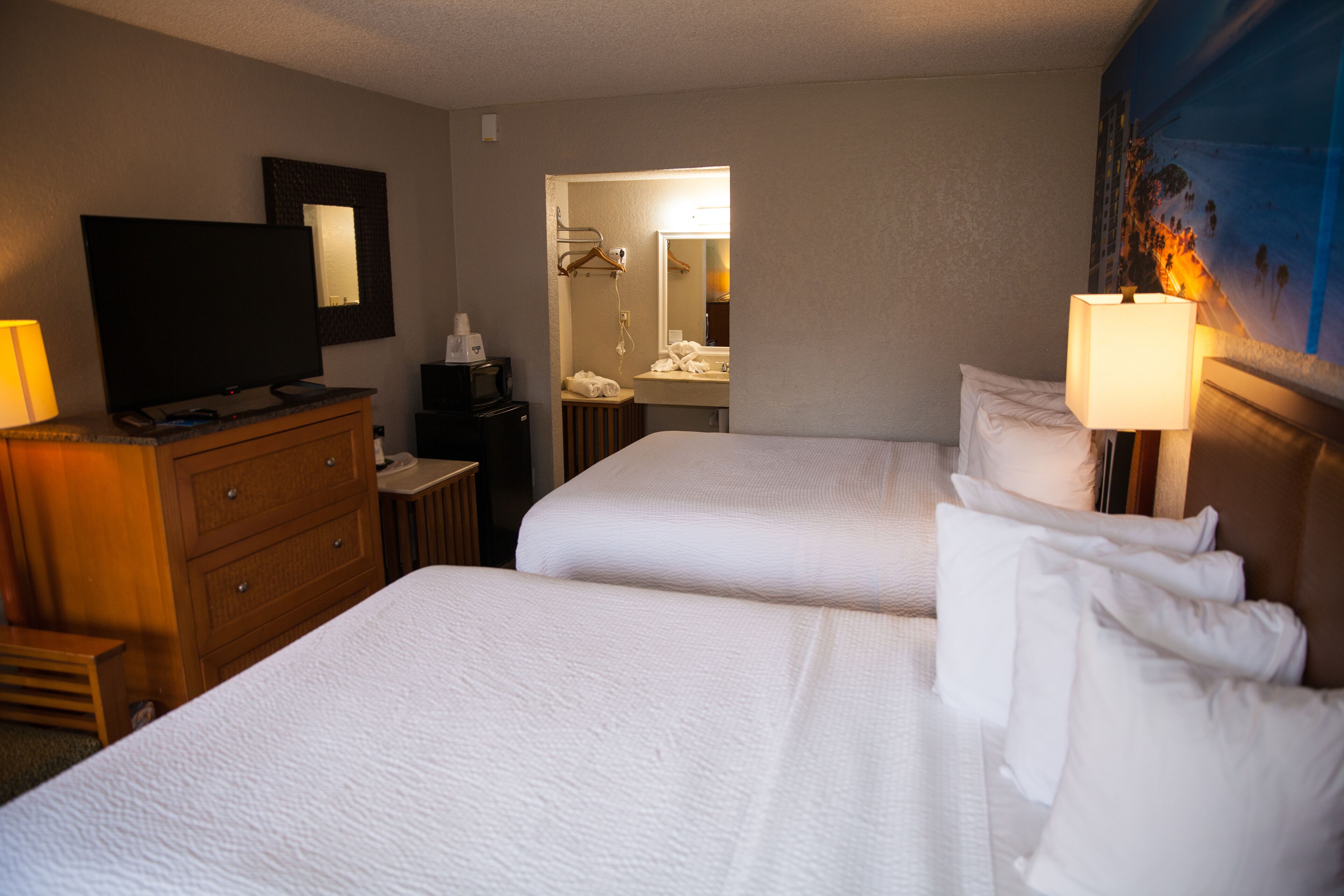 A hotel room with two beds, a TV, a desk, and a bathroom visible through an open door.