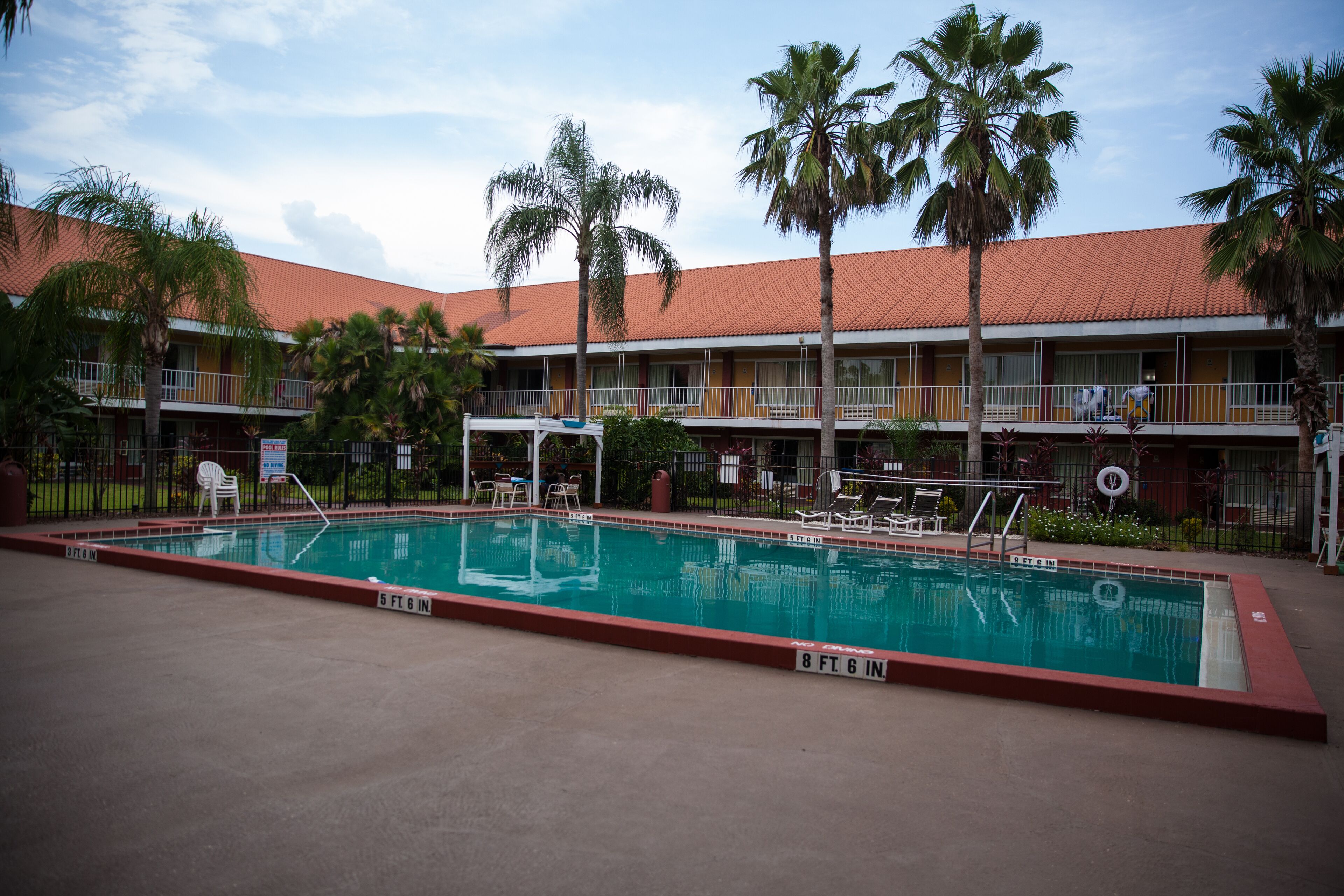 Un hotel con piscina, palmeras y techo de tejas rojas.
