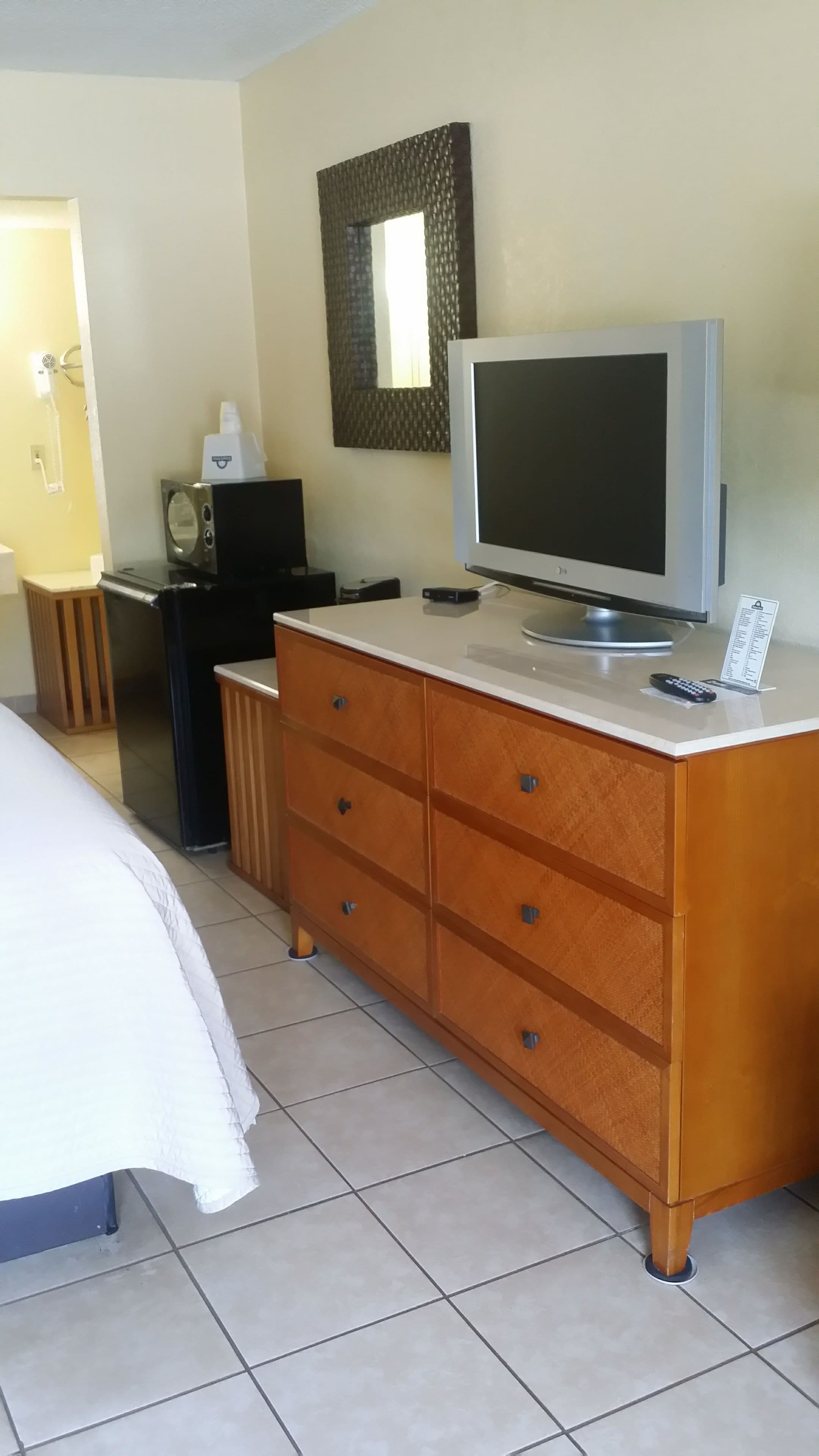 Hotellihuone, jossa on sänky, puinen lipasto, televisio ja pieni pöytä, jonka päällä on kaukosäädin.