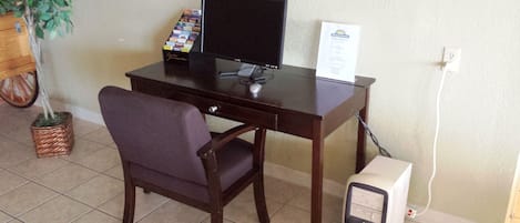 A wooden desk with a computer monitor, a keyboard, and a mouse. There is a chair in front of the desk. A small potted plant is visible to the left of the desk.