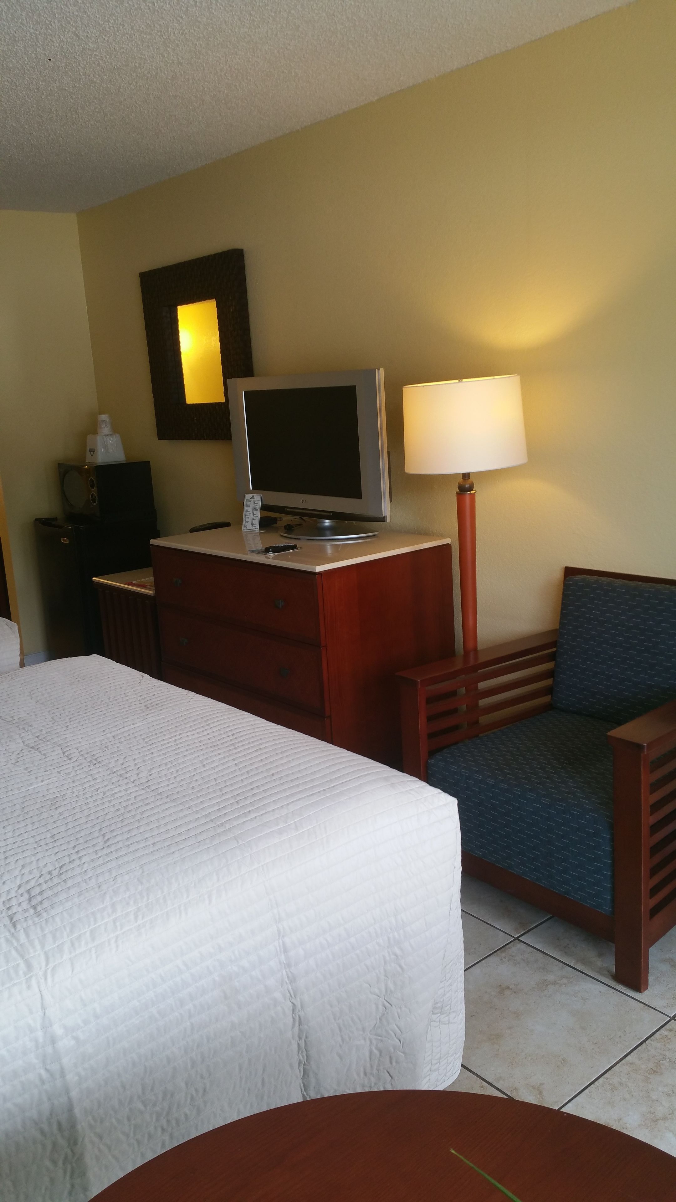 A hotel room with a bed, a desk with a computer, a chair, and a lamp.