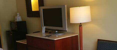 A hotel room with a bed, a desk with a computer, a chair, and a lamp.