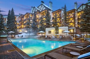A hotel with a pool, lounge chairs, and a snowy landscape.