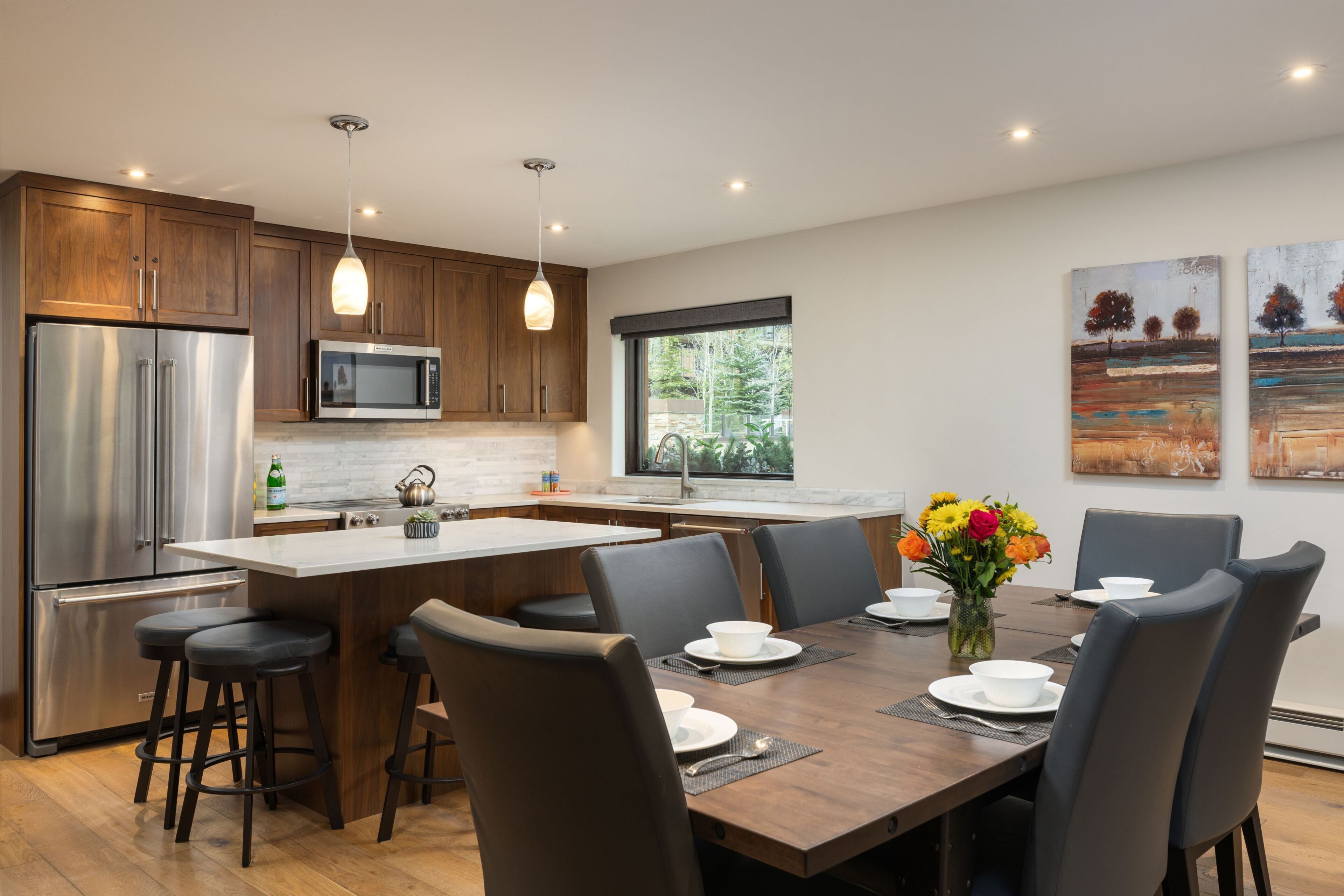 A modern kitchen with stainless steel appliances, a central island with bar stools, and a dining area with a table set for four.