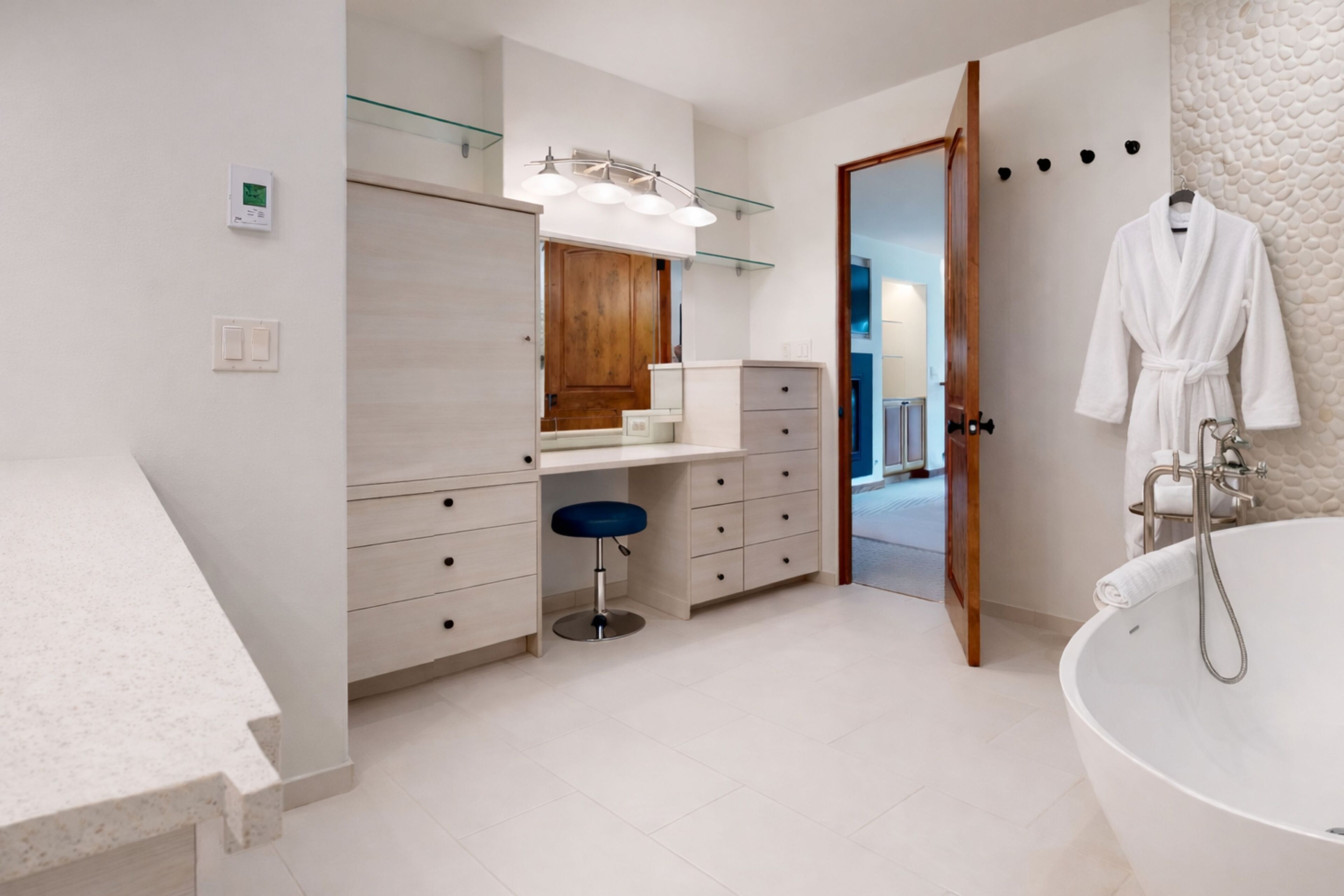 A modern bathroom with a large bathtub, a vanity with a mirror, and a blue stool.