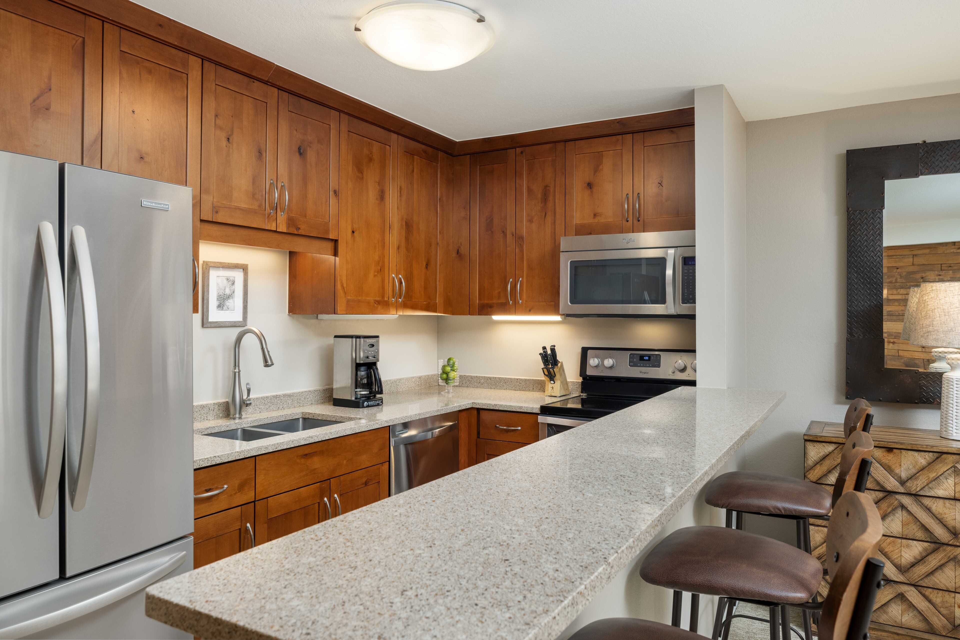 A modern kitchen with wooden cabinets, stainless steel appliances, a granite countertop, and bar stools.
