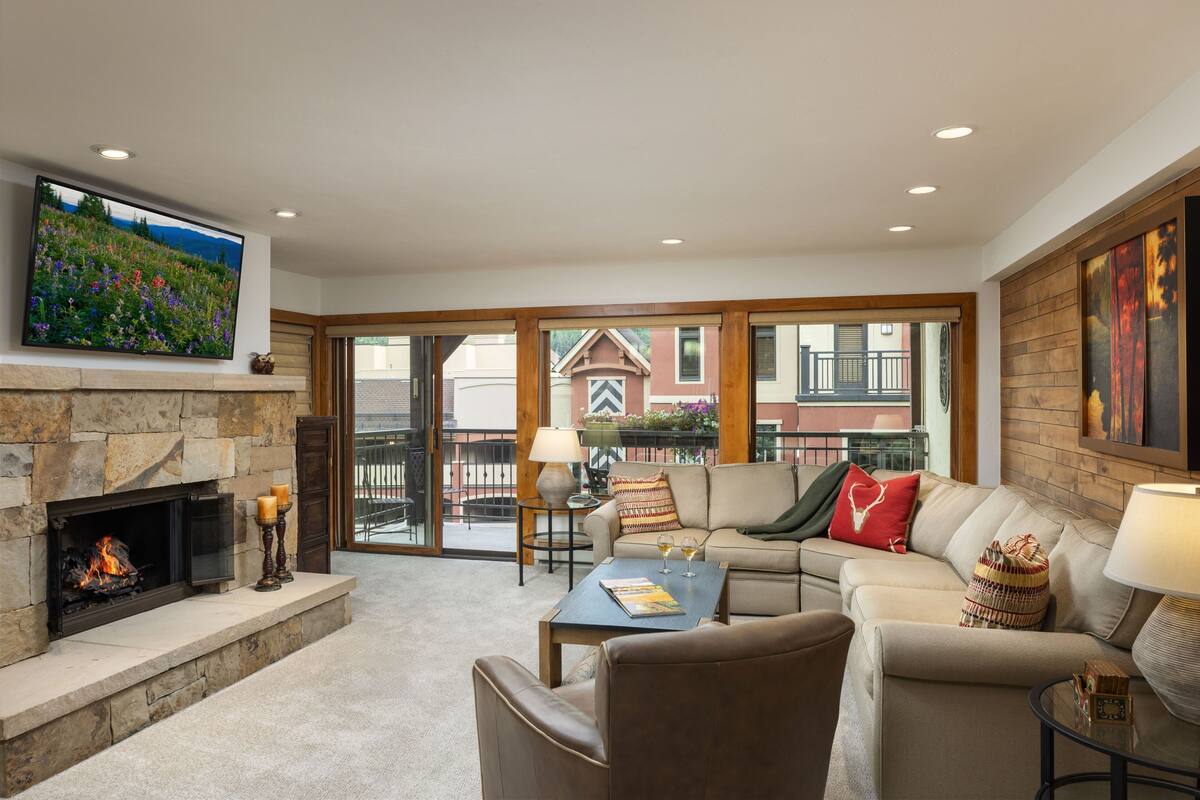 A cozy living room with a fireplace, a sofa, a coffee table, and a TV mounted on the wall.