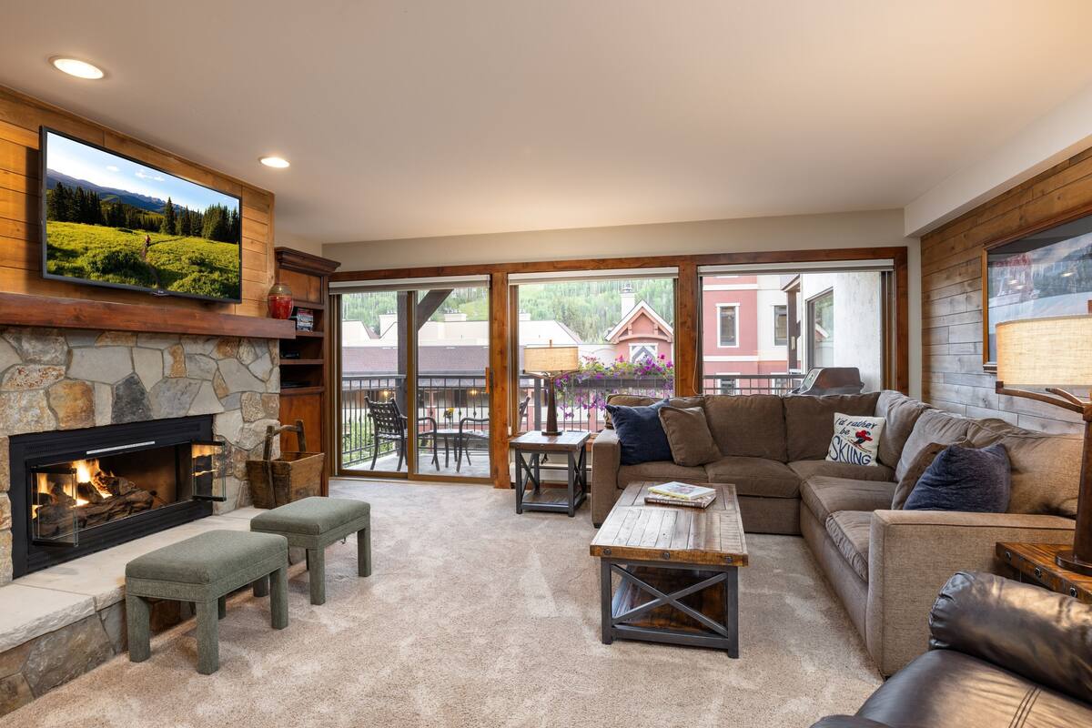 A spacious living room with a stone fireplace, a large flat-screen TV, a cozy sectional sofa, and a wooden coffee table.