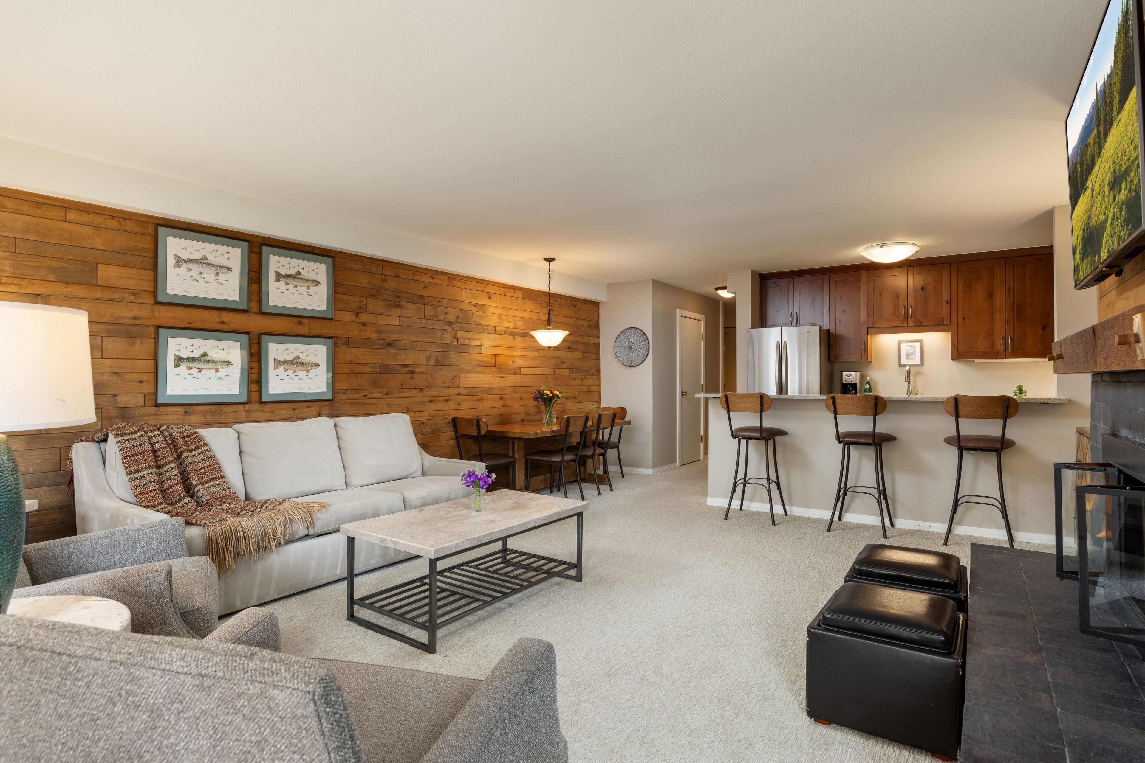 Een moderne woonkamer met een bank, salontafel en voetenbankje, een eethoek met tafel en stoelen, en een keuken met houten kastjes en een koelkast.