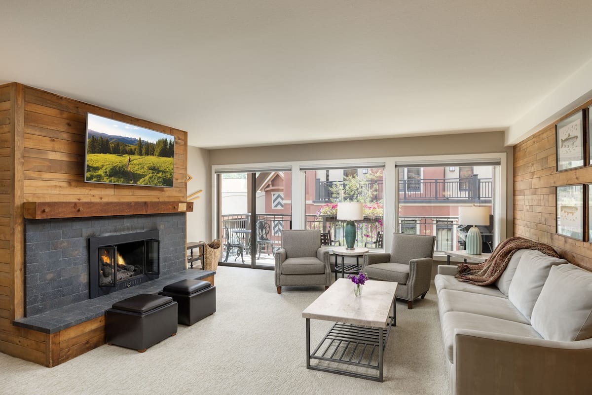 A modern living room with a fireplace, comfortable seating, and large windows offering a view of the outside.