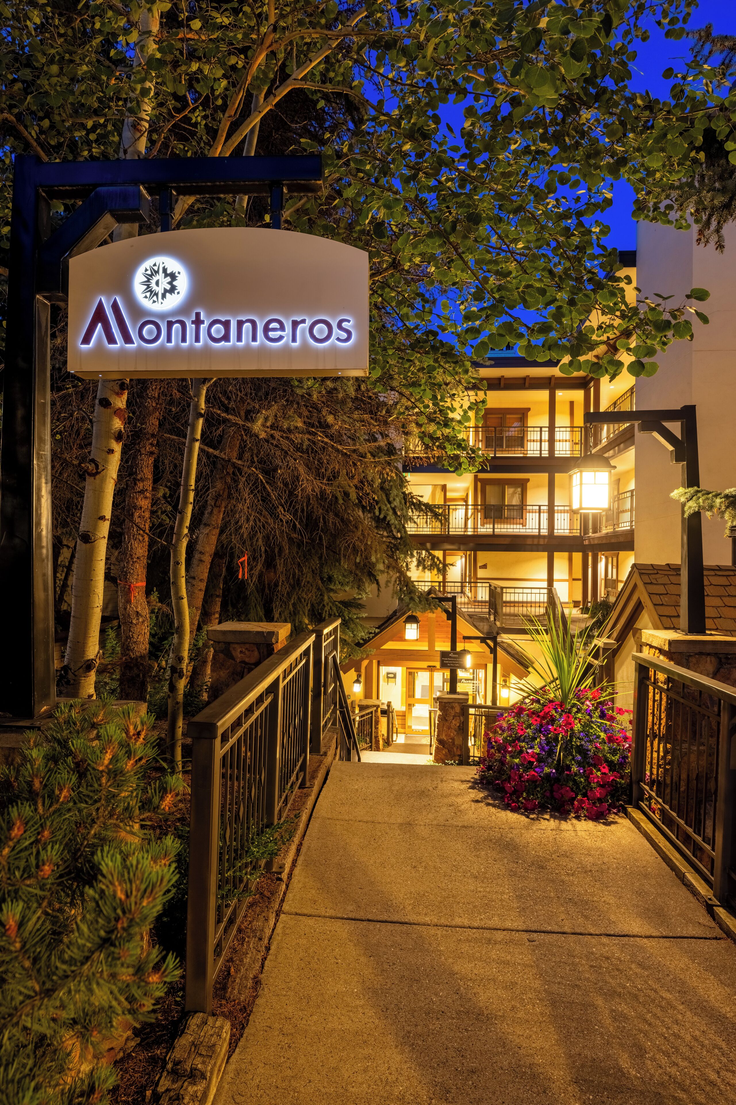 Entrada de un hotel con un cartel, un sendero y un edificio con varios balcones.