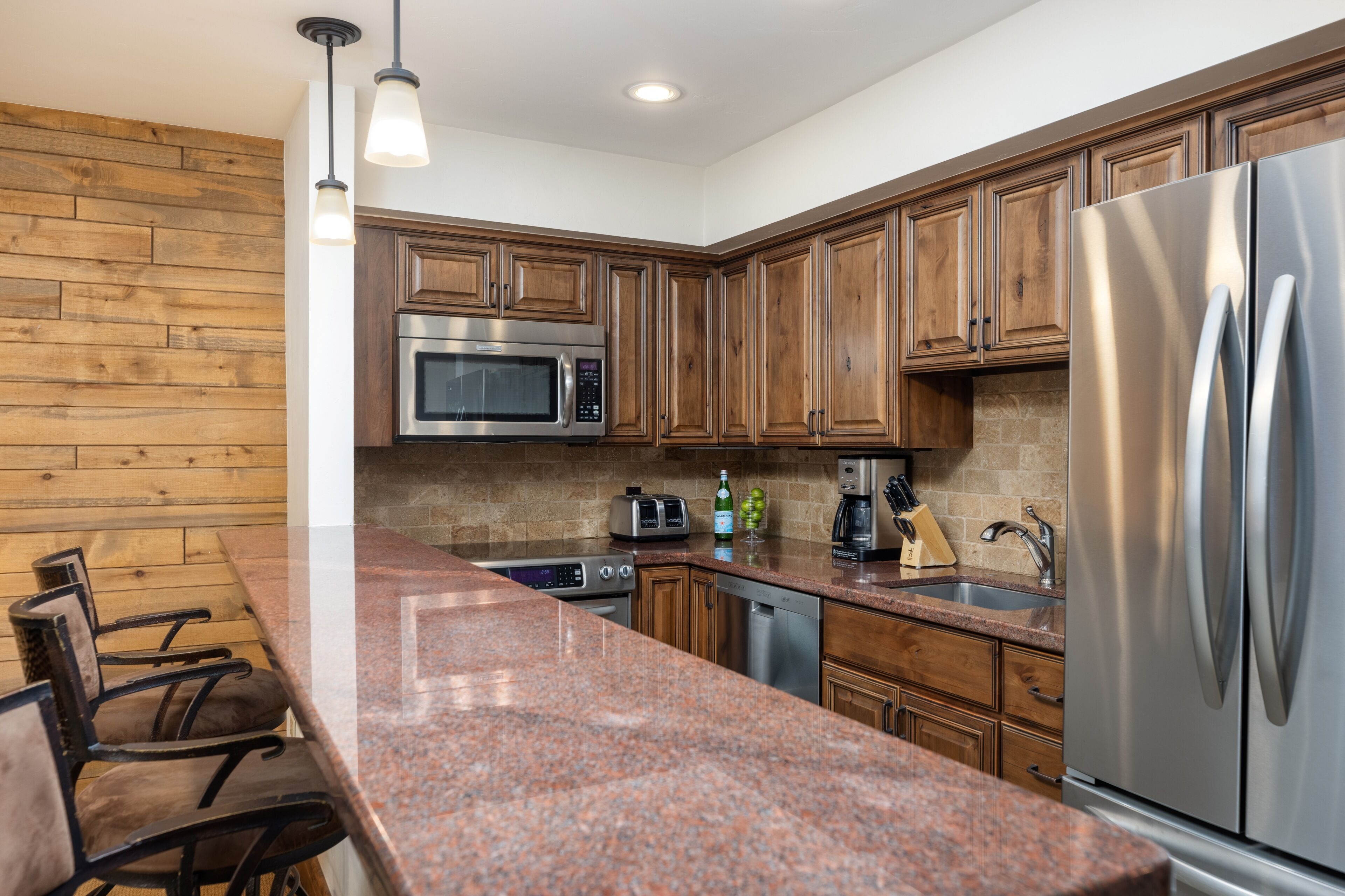 A modern kitchen with wooden cabinets, stainless steel appliances, granite countertops, and pendant lighting.