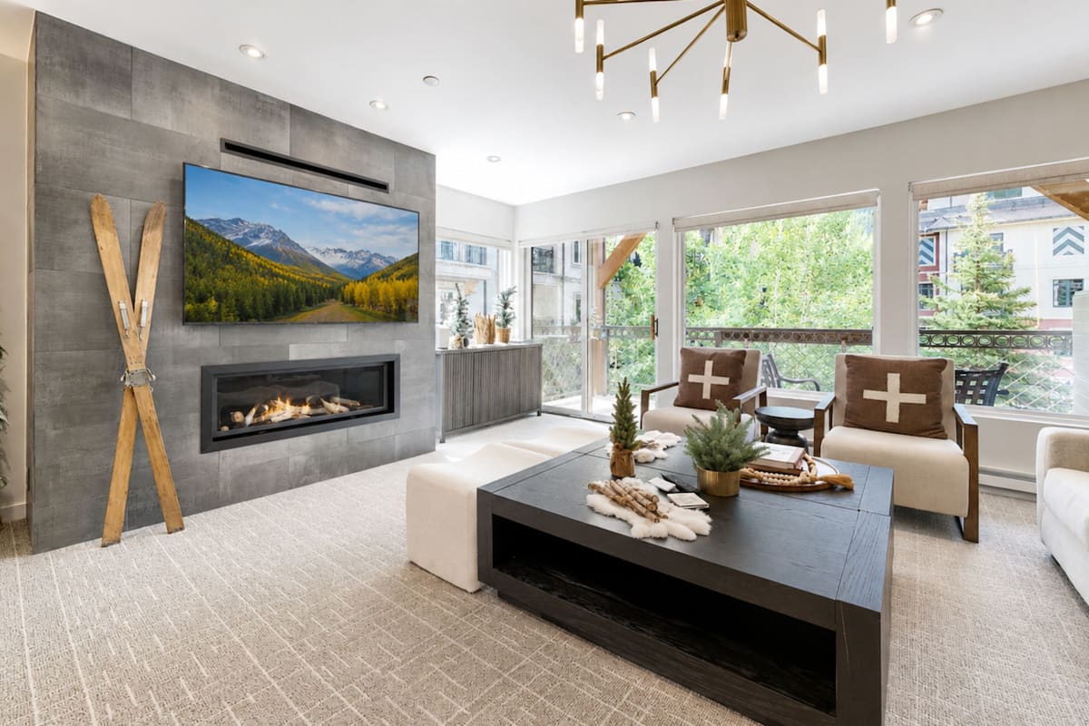 A modern living room with a fireplace, a large TV, and a balcony with a view of the mountains.