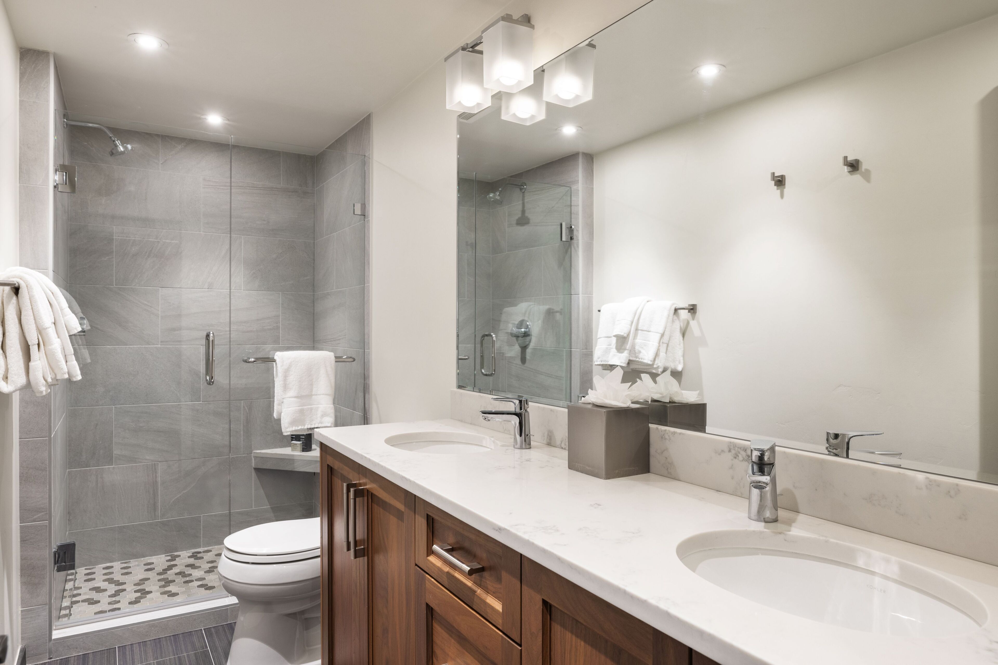 Un baño moderno con un espejo grande, dos lavamanos, una ducha y un inodoro.