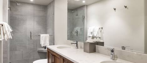 Un baño moderno con un espejo grande, dos lavamanos, una ducha y un inodoro.