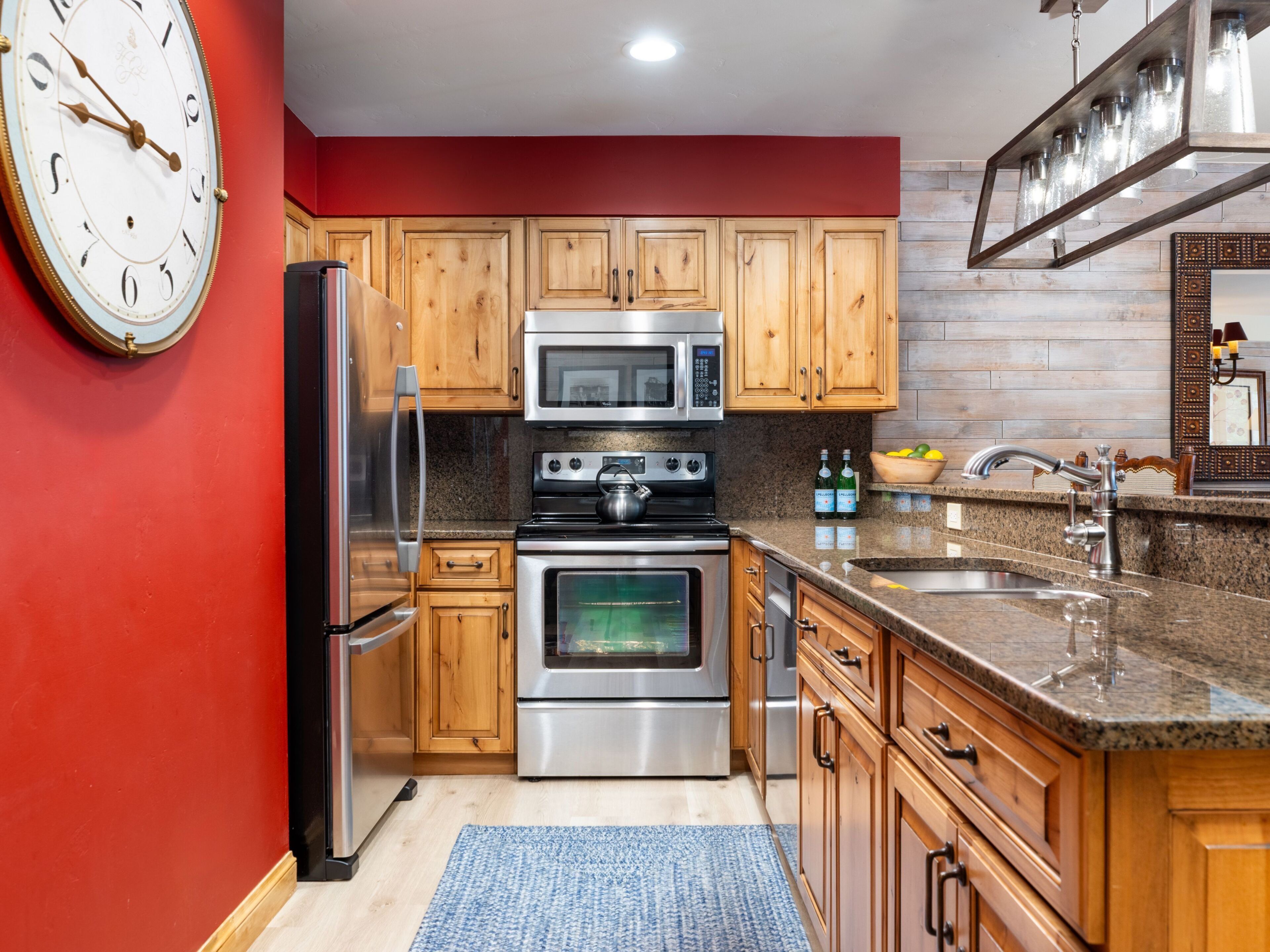 A kitchen with wooden cabinets, stainless steel appliances, a clock, and a granite countertop.