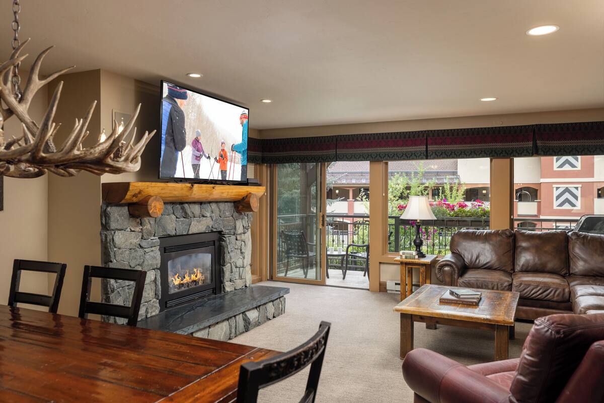 A living room with a stone fireplace, a television, a leather couch, and a dining area.