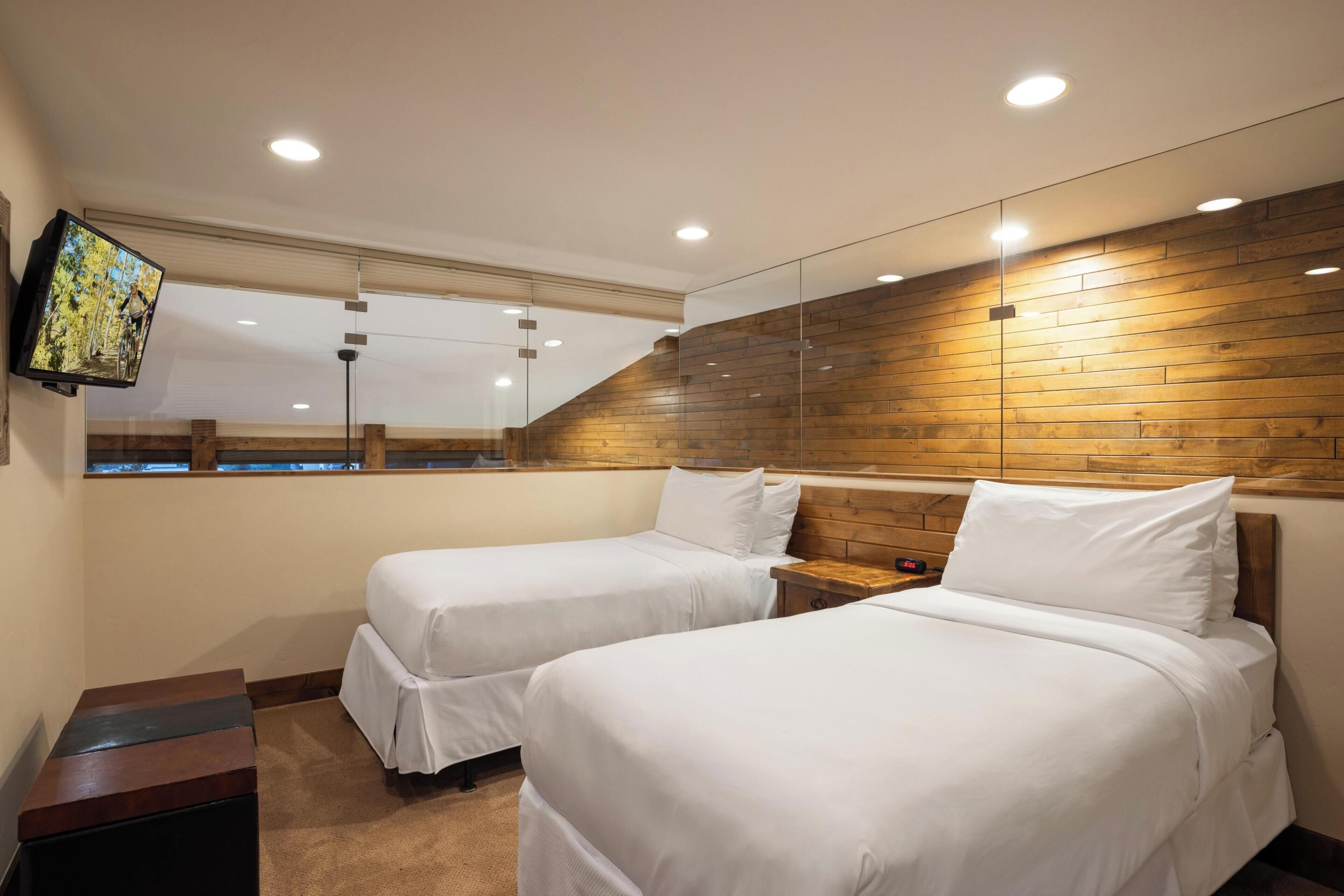 A hotel room with two beds, a TV mounted on the wall, and a wooden accent wall.