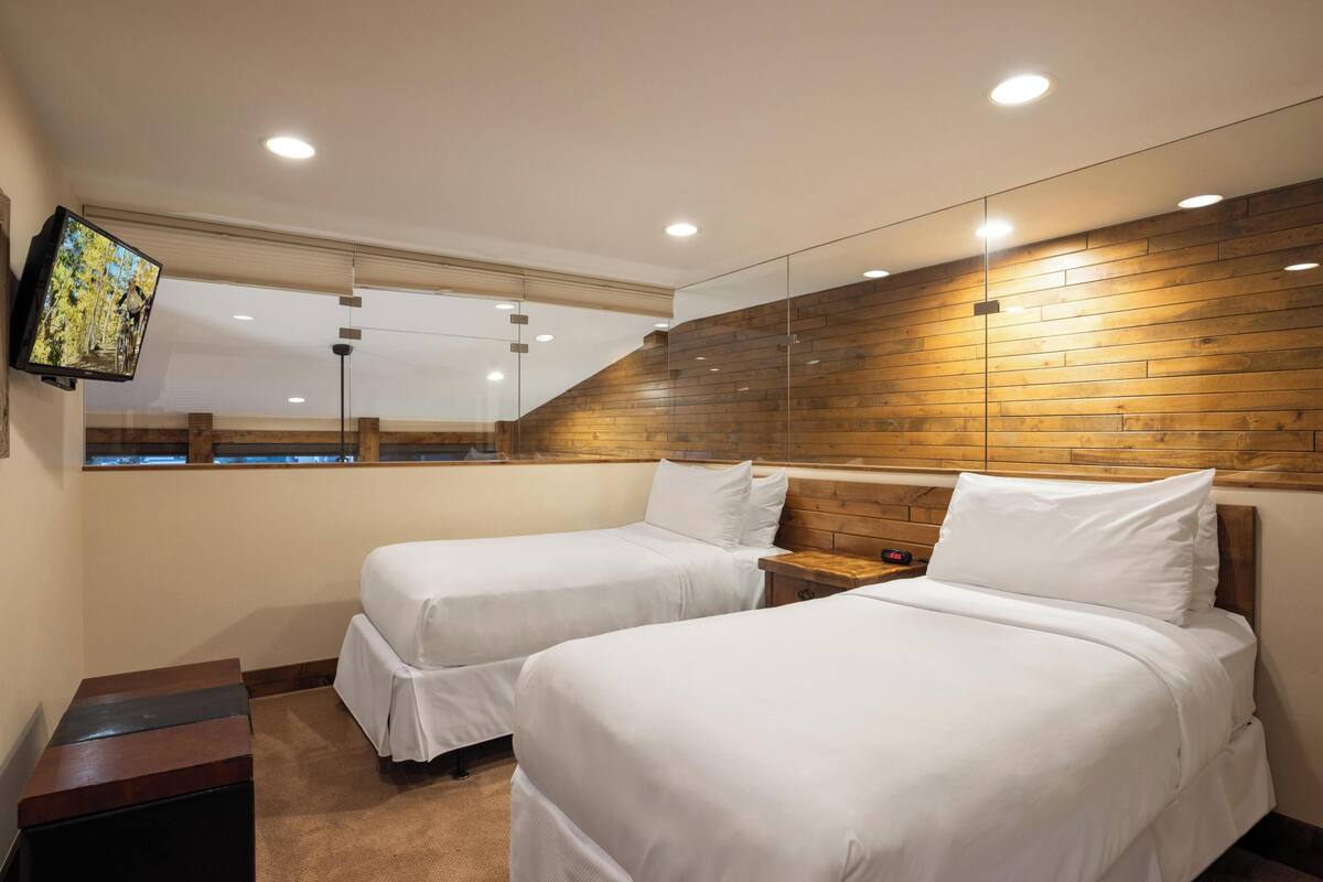 A hotel room with two beds, a TV mounted on the wall, and a wooden accent wall.