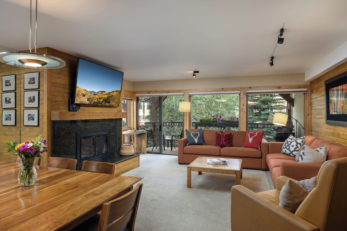 A modern living room with a fireplace, a sofa, a coffee table, and a dining area with chairs and a wooden table.