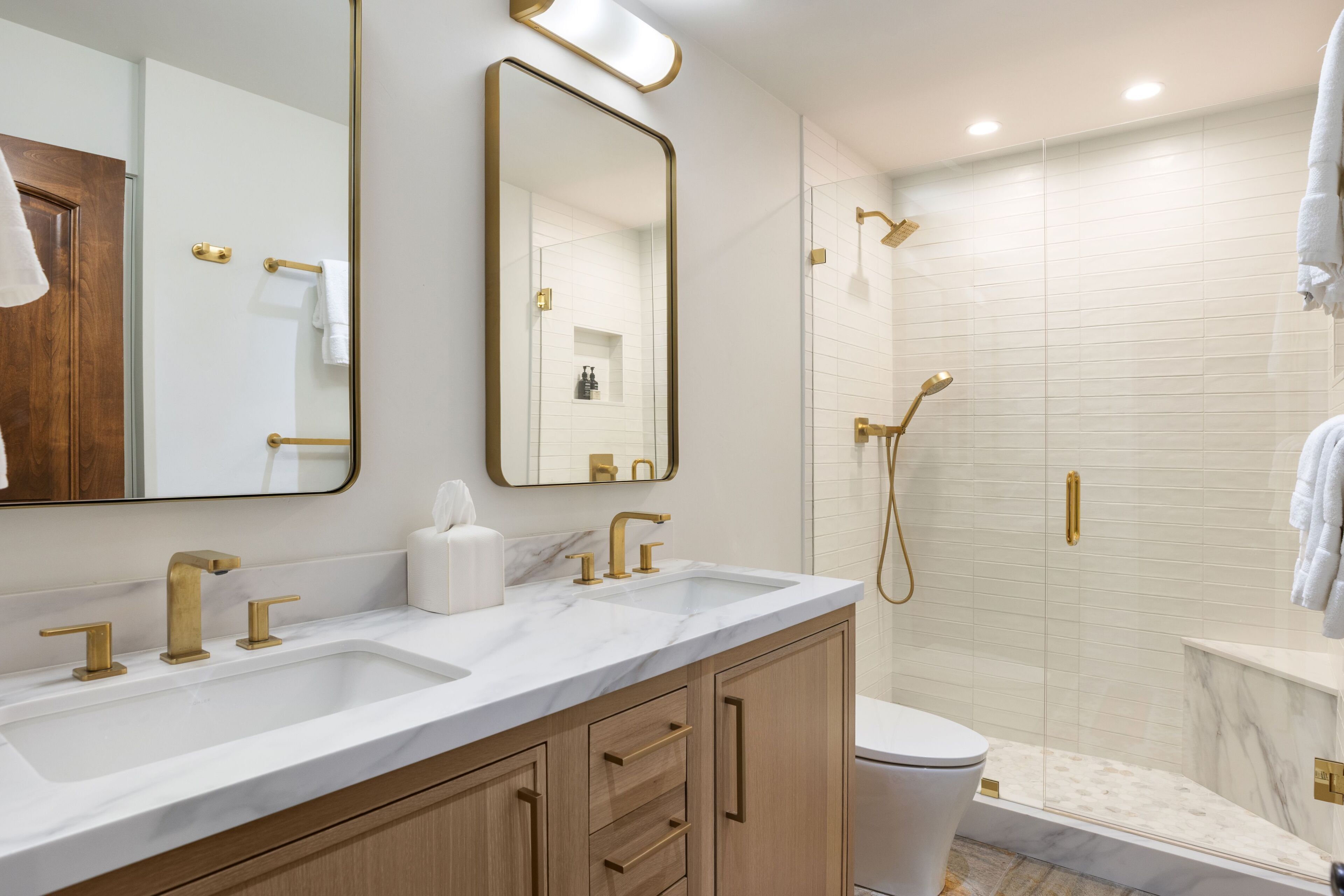 A modern bathroom with a large mirror, two sinks, and a shower.