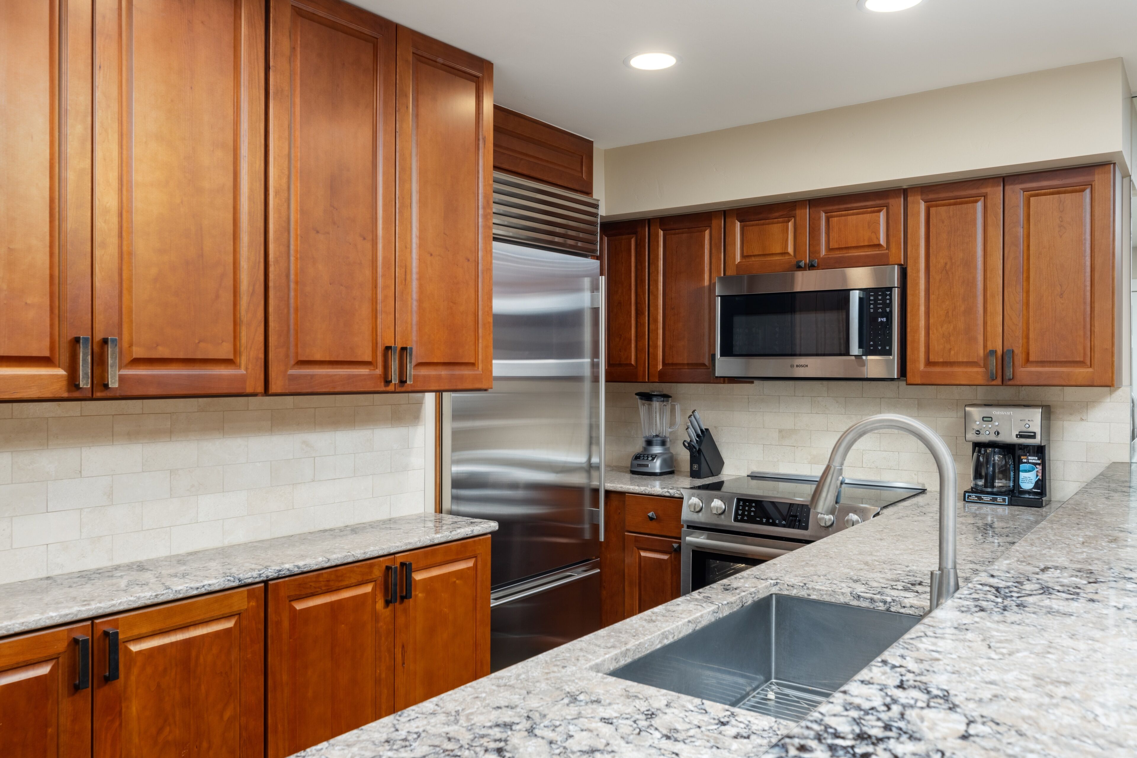 A modern kitchen with wooden cabinets, stainless steel appliances, a granite countertop, and a built-in oven.