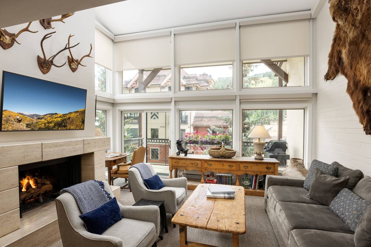 A spacious living room with a fireplace, comfortable seating, and large windows offering views of the outdoors.