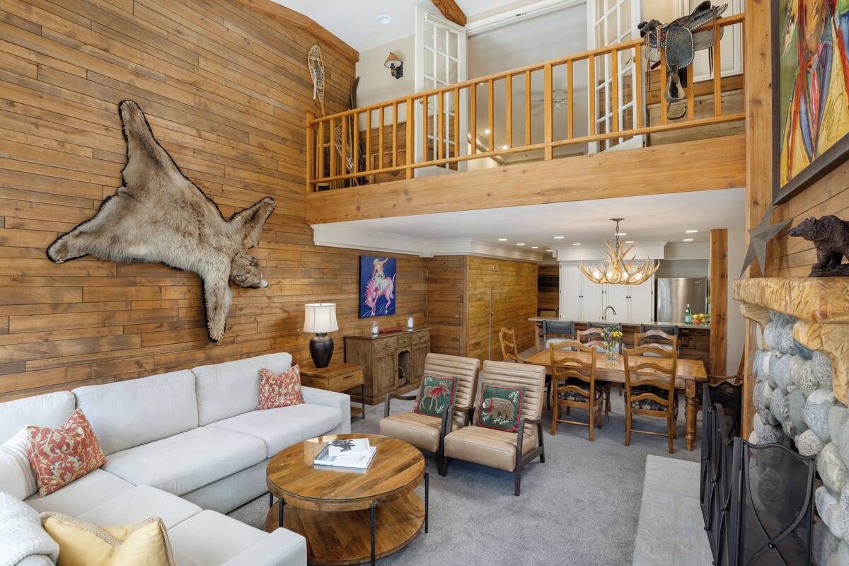A spacious living area with a high ceiling, a wooden staircase, and a dining area.