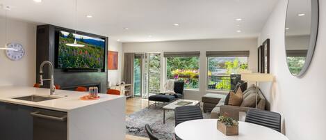 A modern kitchen with a built-in TV, a dining area with a round table, and a living space with a sofa and a coffee table.
