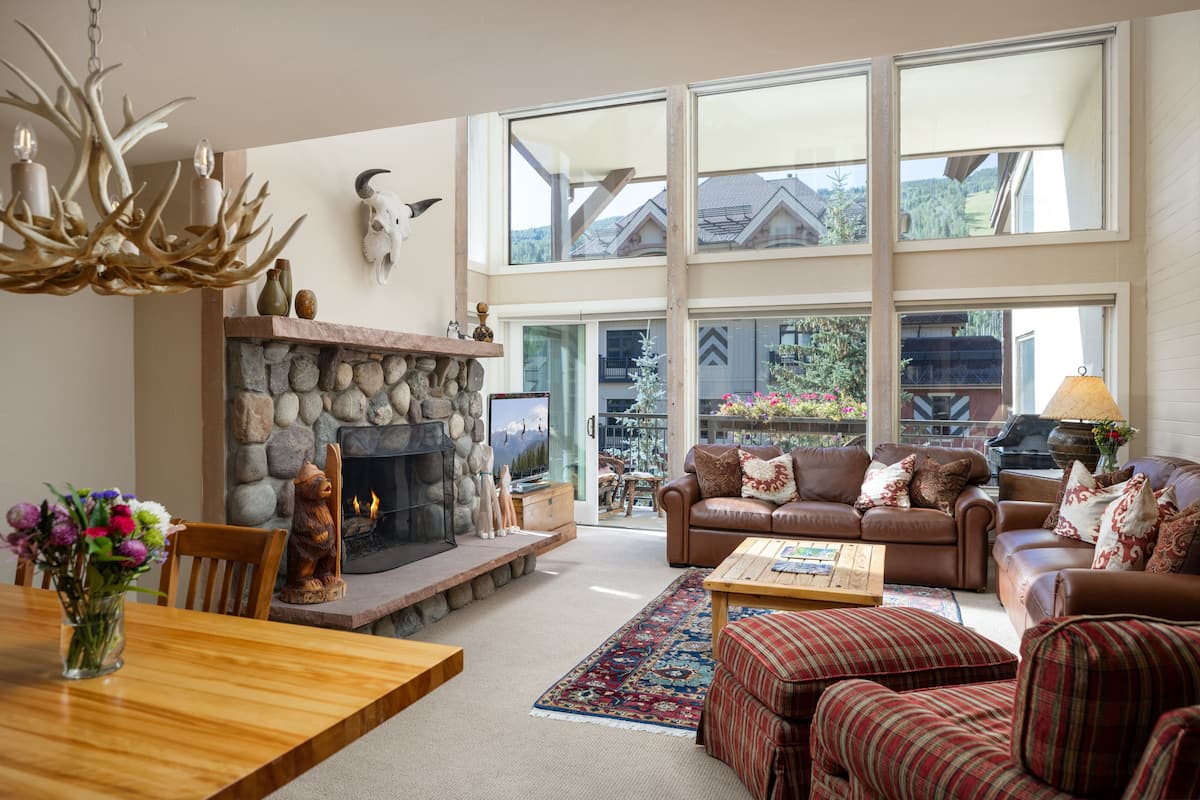 A spacious living room with a stone fireplace, leather sofas, and a large window overlooking a scenic landscape.
